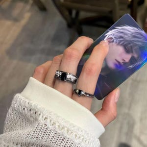 May include: Two black rings with square black gemstones and silver accents. One ring is wider with a larger stone and additional white stones. The other ring is thinner with a smaller stone and a delicate design.