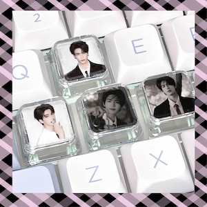 May include: Three clear, square mechanical keyboard keycaps featuring black and white photographic portraits of a young person. The keycaps are positioned among standard white keys with light blue letters Q, E, Z, and X visible on the keyboard.