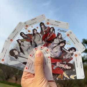May include: A hand holds several clear plastic cards featuring anime-style illustrations of characters in various outfits. Each card has an Instagram-style frame with a profile picture icon, the Instagram logo, and a like counter.