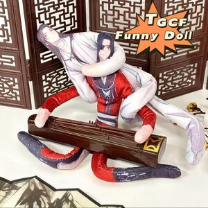 May include: A plush doll featuring two figures in traditional Chinese attire, one in red and white, the other in white. The figures are intertwined, with long, flexible limbs. The doll rests on a brown, rectangular instrument. The text "TGCF Funny Doll" is visible.