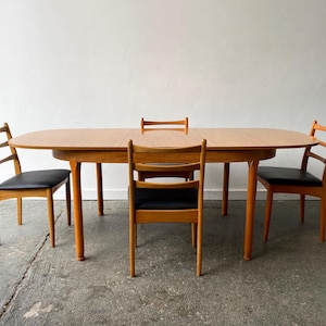 Può includere: Un set da pranzo moderno di metà secolo con un tavolo ovale in legno chiaro e quattro sedie abbinate. Le sedie hanno sedili in pelle nera e un design a schienale a scala. Il tavolo misura circa 152 cm di lunghezza.