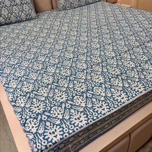 Può includere: Un set di lenzuola a fantasia blu e bianca, composto da un lenzuolo con angoli e due federe. La biancheria da letto presenta un motivo floreale ripetuto. Il letto è fatto e pronto all'uso. Il telaio del letto è rosa chiaro.