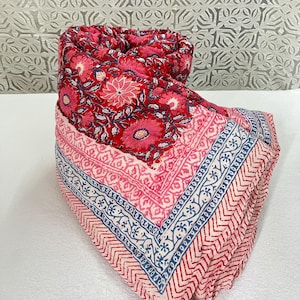 Peut inclure: Une couverture matelassée pliée avec un motif floral dans les tons de rouge et de rose. La bordure présente un motif géométrique en rouge, bleu et blanc. La couverture est en tissu doux et convient à un lit ou un canapé.