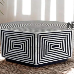 May include: Hexagonal coffee table with a geometric design. The table has a black and white pattern on the top and sides. The sides feature a series of black rectangles within rectangles. The table sits on a black base.