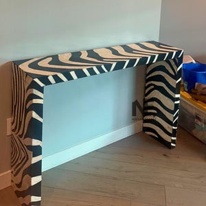 May include: A contemporary console table featuring a zebra stripe design in black and beige. The table is rectangular with a flat surface and two legs. Constructed from wood, it has a polished finish. The table's dimensions are in cm.