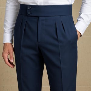May include: Navy blue dress pants with a high waistband and pleats. The pants have a tailored fit and feature two buttons on the waistband. The model is wearing a white dress shirt.