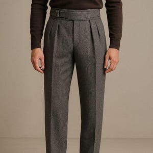 Puede incluir: Pantalones grises de espiga con cintura alta y detalle de cinturón. Los pantalones tienen pliegues y están doblados en los tobillos. El modelo lleva una camisa marrón de manga larga y mocasines de ante marrones.