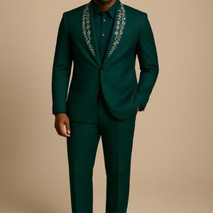 May include: A dark green suit with a matching shirt. The suit jacket has a floral design around the collar. The person is wearing black dress shoes.