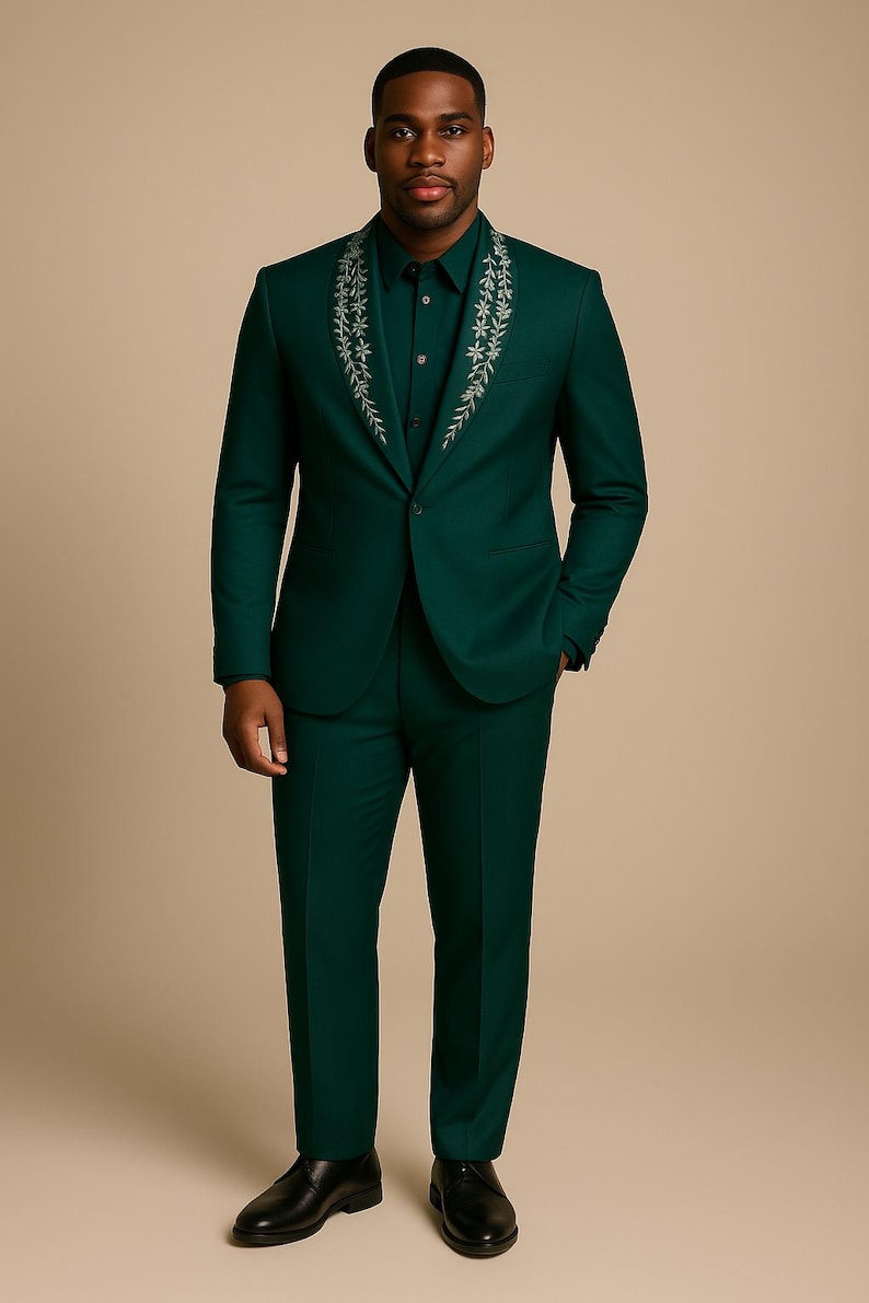 May include: A dark green suit with a matching shirt. The suit jacket has a floral design around the collar. The person is wearing black dress shoes.