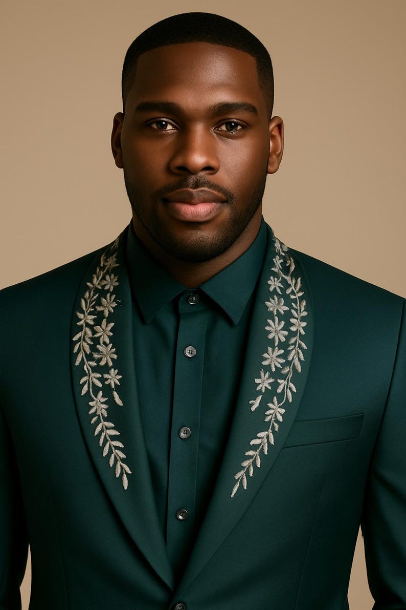 May include: A dark green suit with floral embroidery on the lapel. The suit is worn with a matching green shirt. The image is a close-up of the suit and shirt.