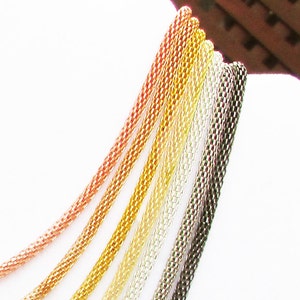May include: A close-up of seven different colored chain necklaces. The chains are made of metal and are arranged in a fan shape. The colors of the chains are rose gold, gold, yellow gold, silver, and black.