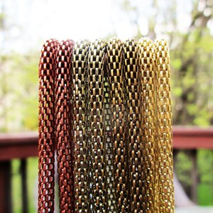 Puede incluir: Primer plano de seis hebras de cadena en diferentes colores met&aacute;licos. Las cadenas est&aacute;n hechas de peque&ntilde;os eslabones cuadrados. Las cadenas est&aacute;n dispuestas en una pila vertical, con la cadena m&aacute;s oscura a la izquierda y la cadena m&aacute;s clara a la derecha.