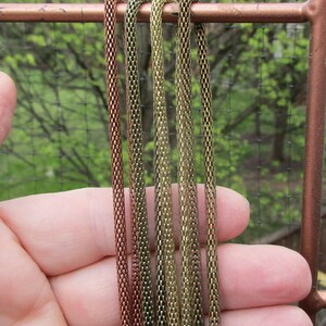Puede incluir: Cinco estilos de cadena diferentes en tonos cobre y oro. Las cadenas est&aacute;n dispuestas verticalmente y se sostienen en una mano.