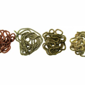 Puede incluir: Cuatro carretes de cord&oacute;n trenzado en diferentes colores: cobre, oro y dos tonos de verde. El cord&oacute;n est&aacute; trenzado y apilado en un mont&oacute;n suelto.