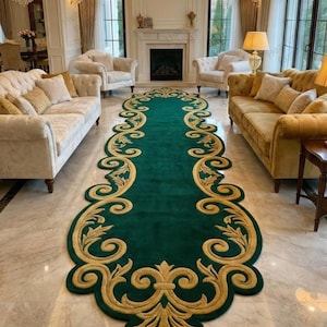 May include: A long, emerald green rug with a gold, ornate border. The rug features a repeating floral and scroll design along its edges. The rug is placed on a marble floor in a living room setting, with sofas and chairs visible in the background.
