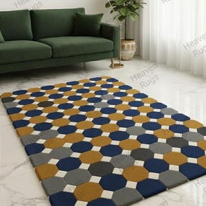 Könnte beinhalten: Rechteckiger Teppich mit einem geometrischen Muster aus sechseckigen Formen in Marineblau, Senfgelb, Grau und Weiß. Der Teppich liegt auf einem Marmorboden vor einem grünen Sofa.