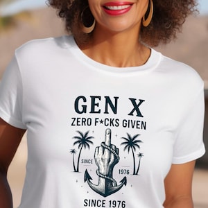 Puede incluir: Camiseta blanca con el texto "GEN X ZERO F*CKS GIVEN SINCE 1976". El diseño incluye una mano haciendo una peineta, palmeras y un ancla. La camiseta es de cuello redondo.