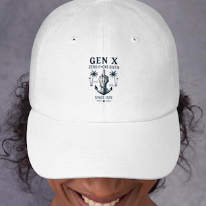 Puede incluir: Gorra de béisbol blanca con visera curva. La gorra presenta un gráfico con el texto "GEN X ZERO F*CKS GIVEN SINCE 1976" y una ilustración de una mano haciendo una peineta, palmeras y un ancla.