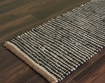 May include: A black and white striped runner rug with a woven texture. The rug has a natural fiber border and is placed on a dark wood floor. The rug's pattern is a series of black and white squares.