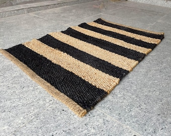 May include: A rectangular rug with alternating black and tan stripes. The rug is made of a woven material, likely jute or a similar natural fiber. The stripes run horizontally across the rug.