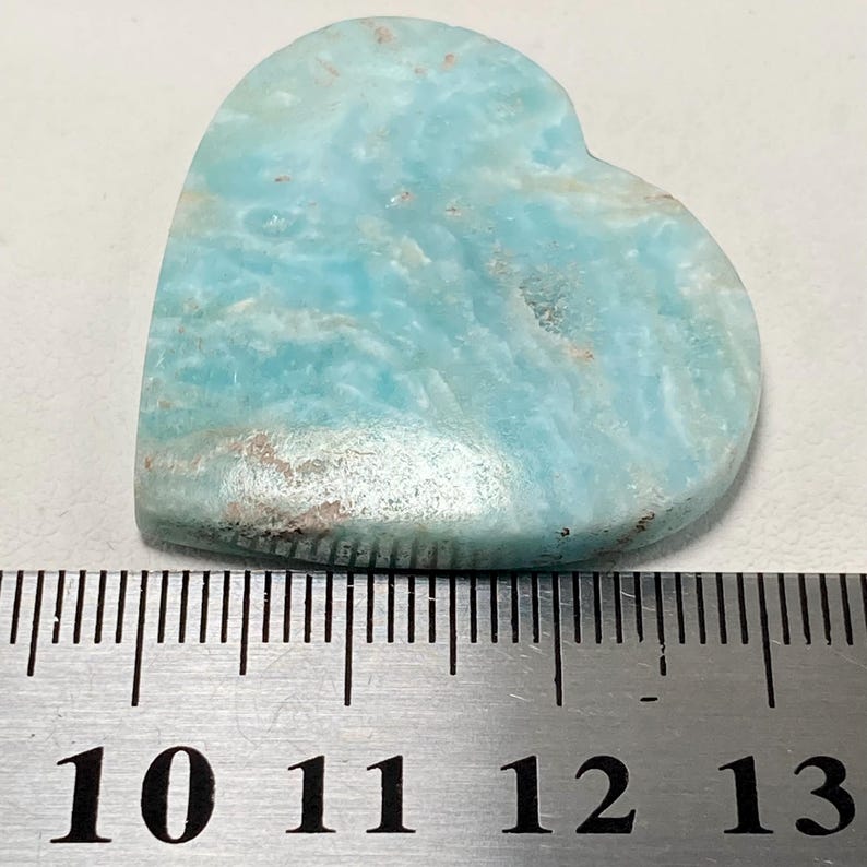May include: A heart-shaped gemstone with a light blue and white marbled pattern. The stone has a smooth, polished surface and measures approximately 5 cm in length. The gemstone is a natural stone.