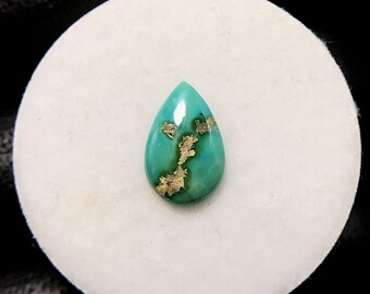 May include: A teardrop-shaped turquoise gemstone with gold-coloured matrix. The polished stone is set against a white background. The gemstone is approximately 2.5 cm in length.