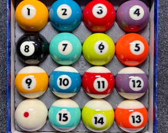 May include: A full set of snooker balls in a blue box. The balls are numbered 1 to 15, featuring colours such as yellow, blue, red, purple, black, green, and orange. The balls are neatly arranged in the box, ready for a game of snooker.
