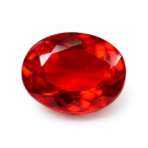 May include: A faceted, oval gemstone in a vivid red colour. The gem's surface reflects light, revealing its internal structure and brilliance. The gemstone is set against a white background, highlighting its colour and clarity. Suitable for jewellery.