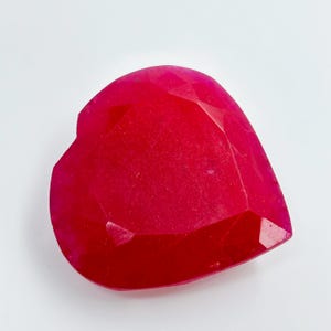May include: A heart-shaped, faceted gemstone in a vibrant shade of red. The gemstone has a polished surface with multiple facets, catching the light. The shape is a classic heart, perfect for jewelry or crafting.