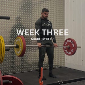 Puede incluir: Una persona realizando un peso muerto con una barra cargada con discos rojos y amarillos. El texto "WEEK THREE MICROCYCLE 2" se muestra en blanco. La persona lleva una camiseta negra de manga larga y pantalones negros.