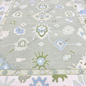 Peut inclure: Un grand tapis rectangulaire avec un fond vert clair et un motif floral répétitif dans les tons de bleu, vert et blanc. Le tapis a une bordure détaillée avec des motifs géométriques.