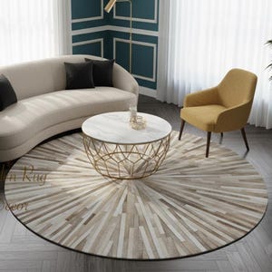 Könnte beinhalten: Ein runder Teppich mit einem Sonnenstrahlenmuster in Beige-, Creme- und Brauntönen, platziert in einem Wohnzimmer mit einem geschwungenen beigen Sofa, schwarzen Kissen, einem senfgelben Sessel und einem runden Couchtisch mit weißer Marmorplatte.