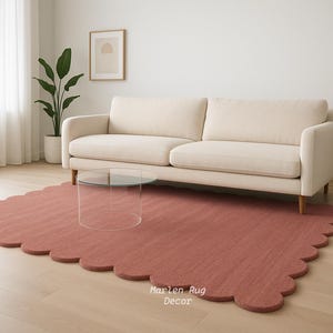 Puede incluir: Un sal&oacute;n con un sof&aacute; crema, una mesa de centro de cristal transparente y una alfombra rosa con borde festoneado. La habitaci&oacute;n tiene suelo de madera y una ventana grande.