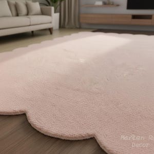 Puede incluir: Una alfombra grande de color rosa claro con un borde festoneado. La alfombra tiene una superficie suave y texturizada y est&aacute; colocada sobre un suelo de madera. Las palabras "Marten Rug Decor" est&aacute;n impresas en la esquina inferior derecha.