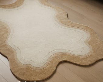 May include: A beige, cloud-shaped rug with a layered design. The rug features a light beige center, surrounded by concentric borders of varying shades of beige and tan. The text "Marlen Rug Decor" is visible.