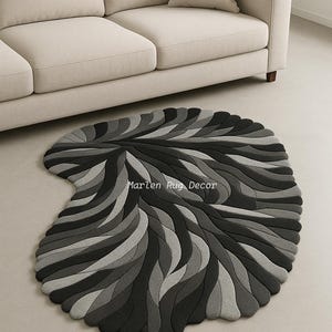 May include: A gray and black area rug with a unique, organic shape. The rug features a layered design of curved lines in varying shades of gray and black. The text "Marlen Rug Decor" is visible on the rug.