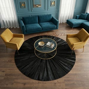 Könnte beinhalten: Ein Wohnzimmer mit teal-farbenen Sofas und senffarbenen Sesseln. Ein runder, schwarzer Teppich mit plissiertem Design liegt unter einem Couchtisch mit Glasplatte und goldenem Rahmen. Der Raum hat teal-farbene Wände und goldene Akzente.