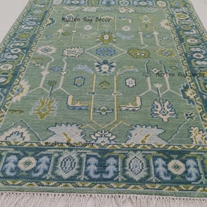 May include: A rectangular, light green rug with a detailed floral pattern in shades of blue, white, and green. The rug has a dark blue border and white fringe along the bottom edge. The text "Marlen Rug Decor" is printed on the rug.