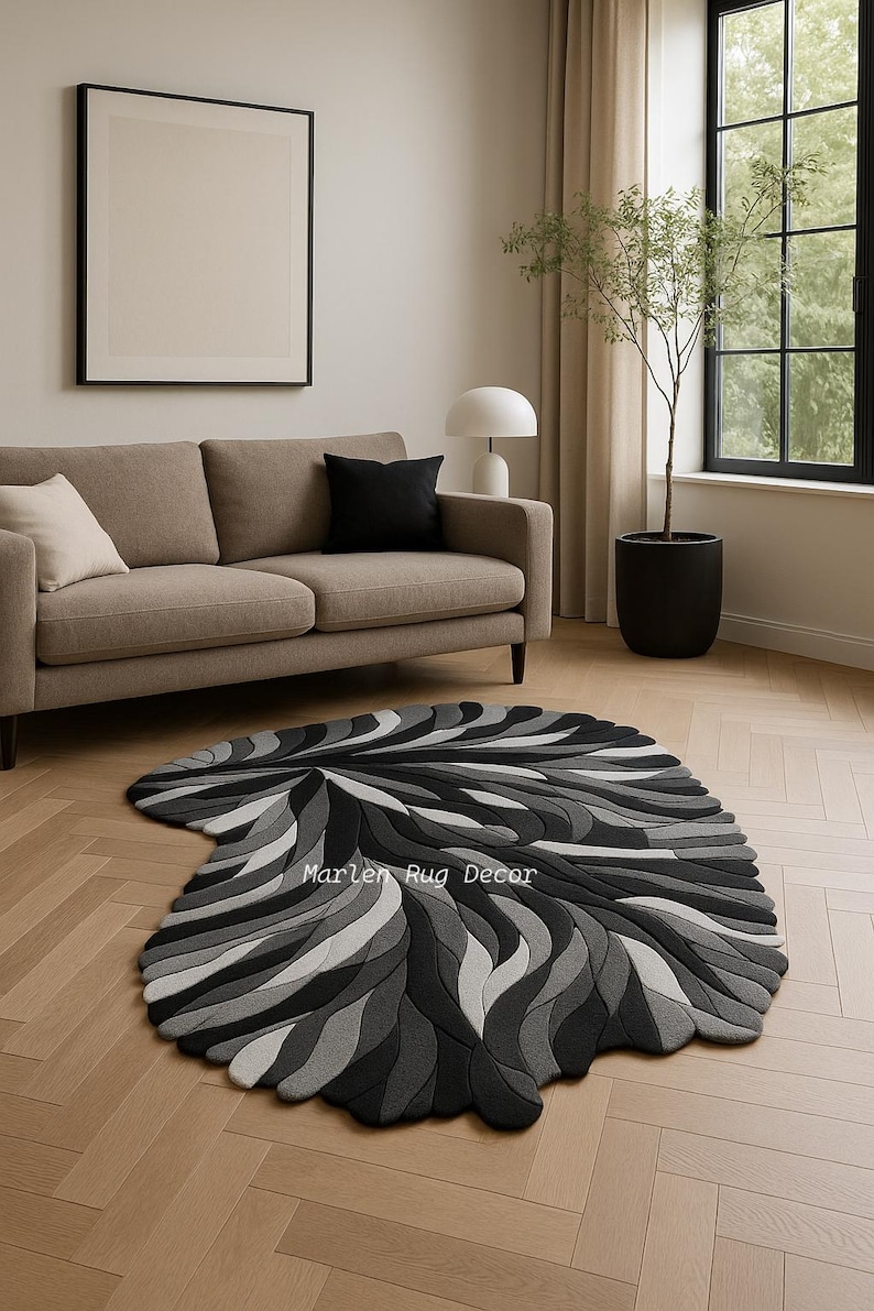 May include: A modern, abstract rug in shades of gray and black, with a swirling, organic pattern. The rug is placed on a light-colored wooden floor in a living room setting. The text "Marlen Rug Decor" is visible on the rug.