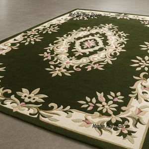May include: A rectangular green rug with an ornate floral design. The rug features a cream-colored border with floral and scrollwork patterns. The central design is a cream-colored medallion with pink accents. The rug is a decorative floor covering.