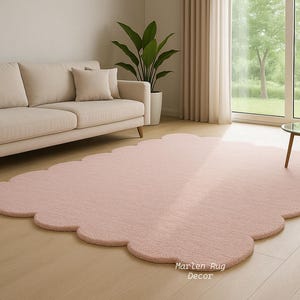 Puede incluir: Una alfombra rosa claro con bordes festoneados en un sal&oacute;n. Un sof&aacute; beige con cojines est&aacute; en el fondo, junto con una peque&ntilde;a mesa redonda y una planta en maceta. La alfombra est&aacute; sobre un suelo de madera.