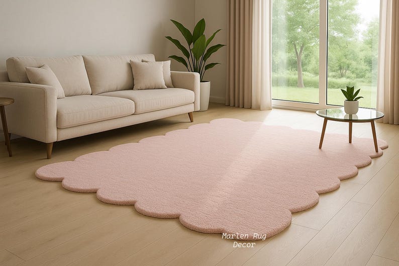 Puede incluir: Una alfombra rosa claro con bordes festoneados en un sal&oacute;n. Un sof&aacute; beige con cojines est&aacute; en el fondo, junto con una peque&ntilde;a mesa redonda y una planta en maceta. La alfombra est&aacute; sobre un suelo de madera.