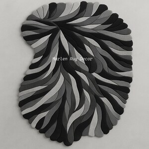 May include: A decorative rug with a unique, abstract design. The rug features a pattern of layered, curved shapes in shades of gray and black. The text "Marlen Rug Decor" is visible on the rug.