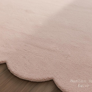 Puede incluir: Primer plano de una alfombra rosa claro con un borde festoneado. La alfombra tiene una superficie texturizada y est&aacute; hecha de un material suave. La alfombra es de color neutro y complementar&iacute;a muchos estilos de decoraci&oacute;n.