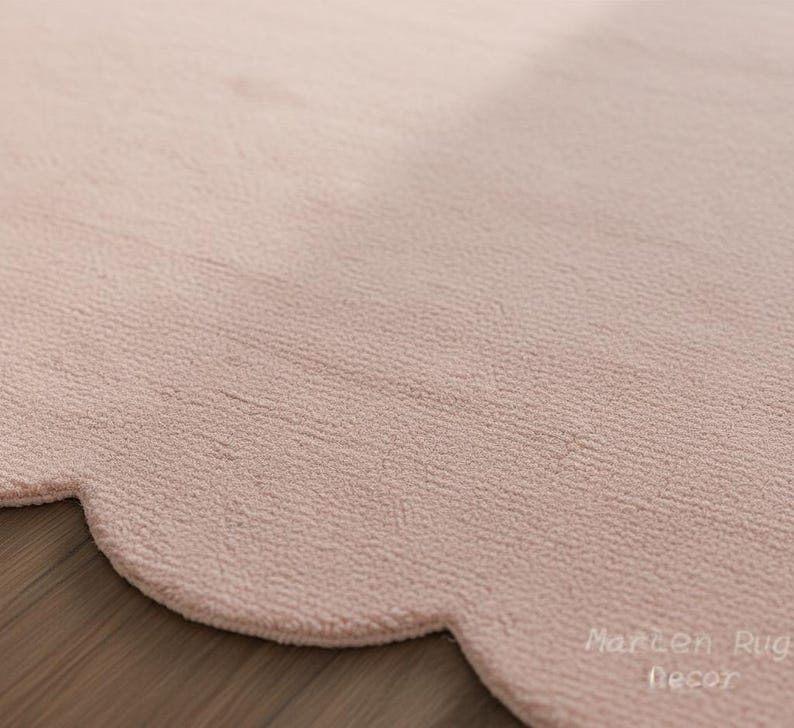 Puede incluir: Primer plano de una alfombra rosa claro con un borde festoneado. La alfombra tiene una superficie texturizada y est&aacute; hecha de un material suave. La alfombra es de color neutro y complementar&iacute;a muchos estilos de decoraci&oacute;n.