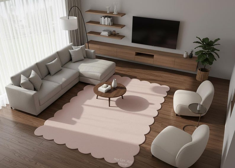 Puede incluir: Un sal&oacute;n moderno con un sof&aacute; esquinero gris claro, dos sillones color crema y una mesa de centro redonda. Una gran alfombra rosa rubor con bordes festoneados ancla el espacio. Un televisor de pantalla plana est&aacute; montado en una consola de madera.