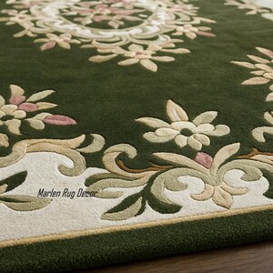 May include: Close-up of a green rug with an intricate floral design. The rug features a central medallion and border with cream, pink, and beige accents. The text "Marlen Rug Decor" is visible.