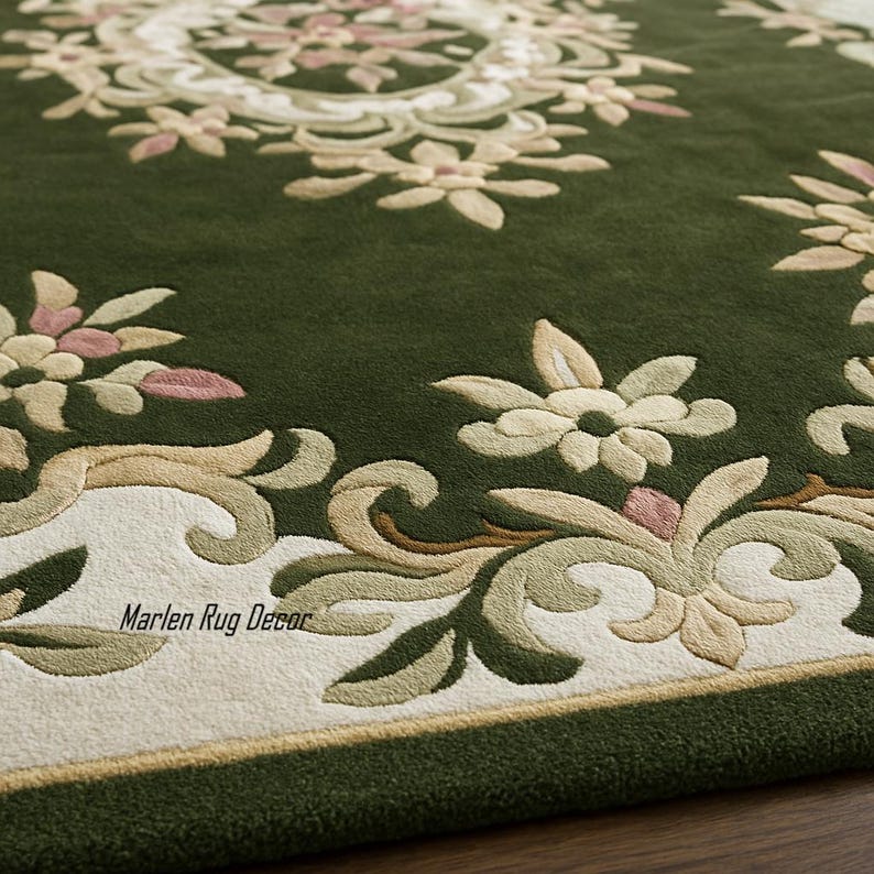 May include: Close-up of a green rug with an intricate floral design. The rug features a central medallion and border with cream, pink, and beige accents. The text "Marlen Rug Decor" is visible.