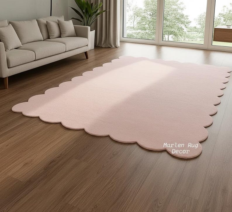 Puede incluir: Una alfombra grande, de color rosa claro, con borde festoneado se muestra sobre un suelo de madera. La alfombra est&aacute; en un sal&oacute;n, con un sof&aacute; y una ventana visibles en el fondo. El texto "Marlen Rug Decor" est&aacute; impreso en la alfombra.