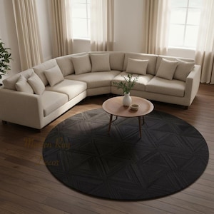 Può includere: Un divano componibile beige con cuscini e un tappeto rotondo grigio scuro con un motivo geometrico. Un tavolino in legno e una pianta in vaso sono anch'essi nella stanza. Il tappeto misura circa 240 cm di diametro.